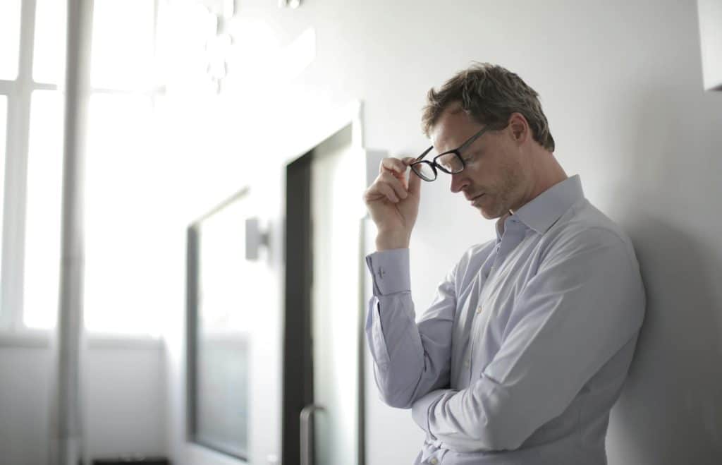 A man in a light blue shirt looking down and holding his glasses, suggesting contemplation or stress related to ADHD and anxiety challenges.