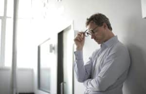 A man in a light blue shirt looking down and holding his glasses, suggesting contemplation or stress related to ADHD and anxiety challenges.