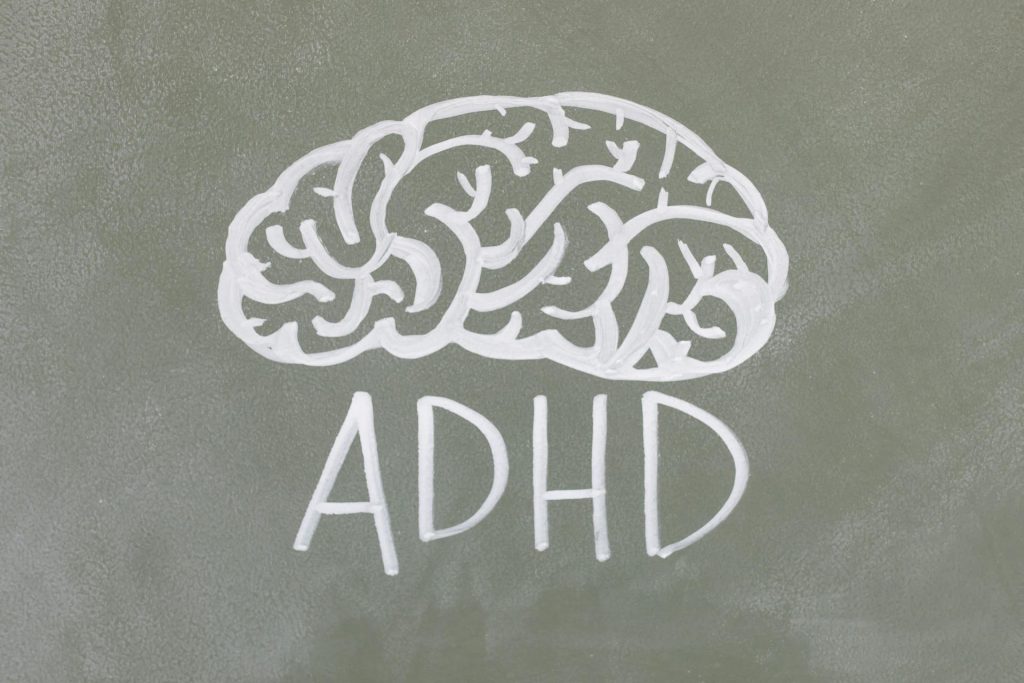 Chalk drawing of a brain above the letters 'ADHD' on a green chalkboard, visually representing the topic of ADHD and its connection to cognitive processes, relevant for discussions on inattentive ADHD and anxiety.