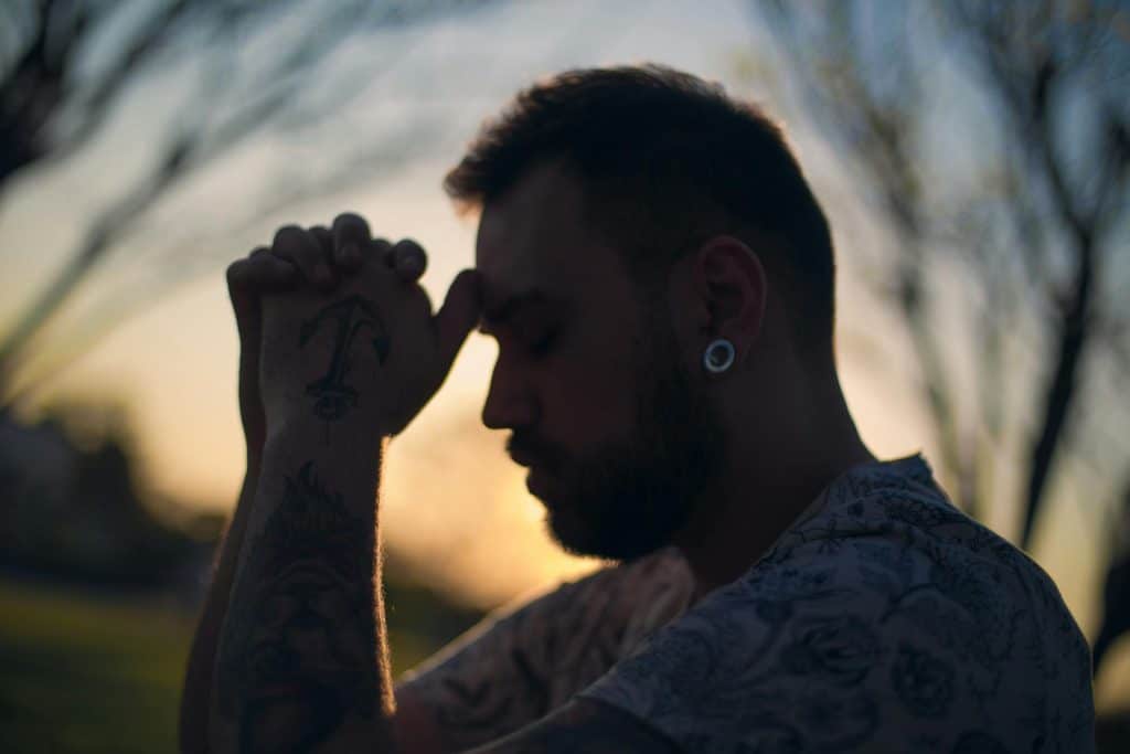 A man with his eyes closed and hands clasped, resting on his forehead. The image symbolizes the internal burden of resentment and silent stress in men's relationships.