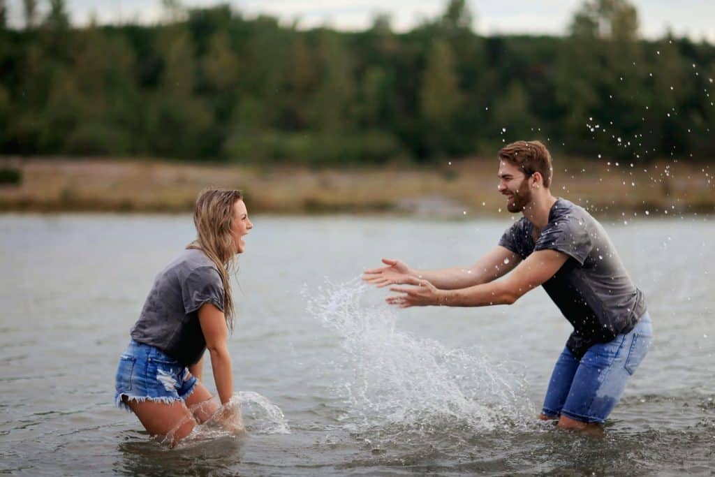 A joyful man and woman laughing and splashing water, representing healthy connection and healing from resentment in relationships.
