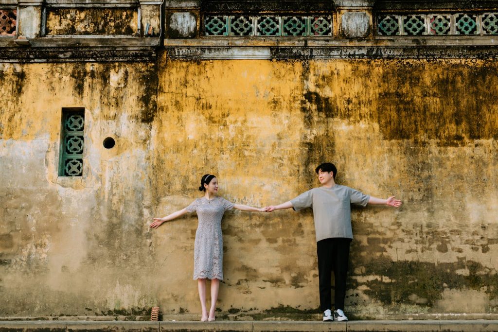 A man and a woman holding hands with their arms outstretched in front of a wall, symbolizing open communication and connection in relationships.